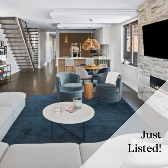Open-plan living room with blue seating, stone fireplace, and adjoining kitchen.